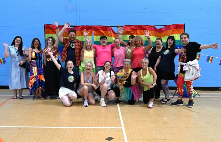 The Pride Zumba group poses in front of rainbow flags in Cheadle