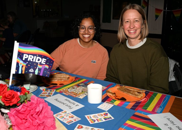 Two people sit at a table decorated with Pride flags at the Endon event