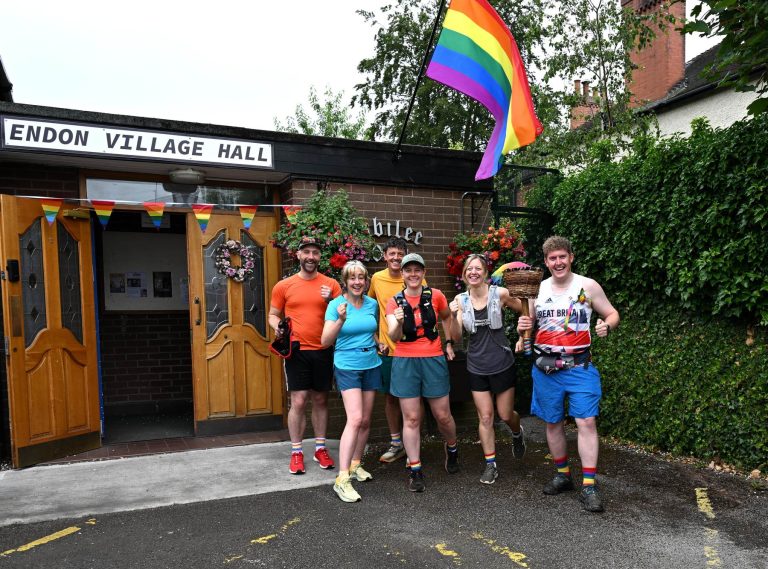 Runners pose outside Endon Village Hall under a rainbow flag