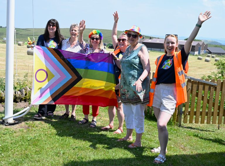 A group cheers and waves beside the Progress Pride flag at Flash
