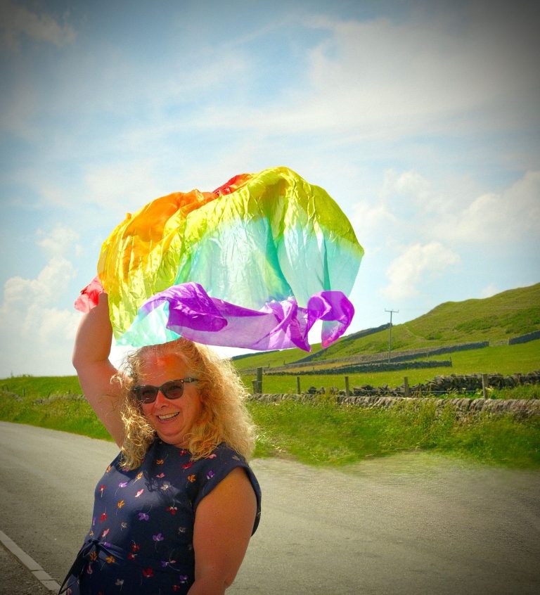 A woman holds a rainbow silk scarf up to the sky at Flash