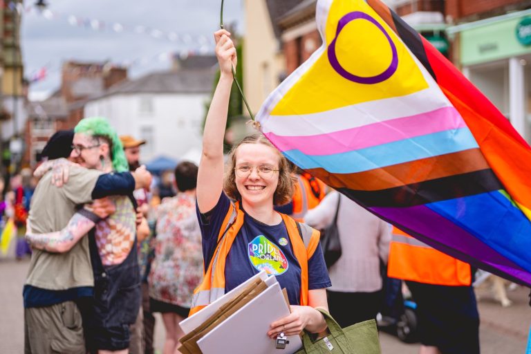 A volunteer waves the Intersex-inclusive Progress Pride flag in Leek