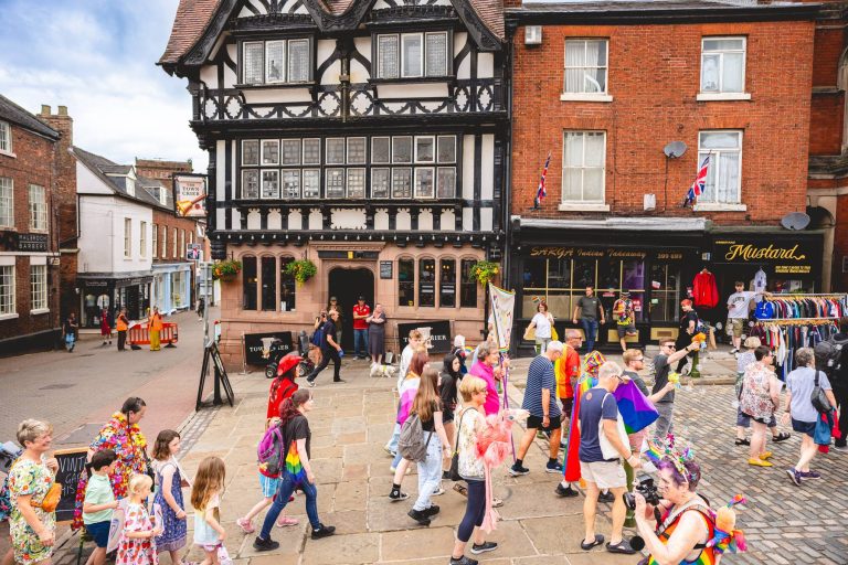 The parade fills the street in front of a black-and-white Tudor building in Leek