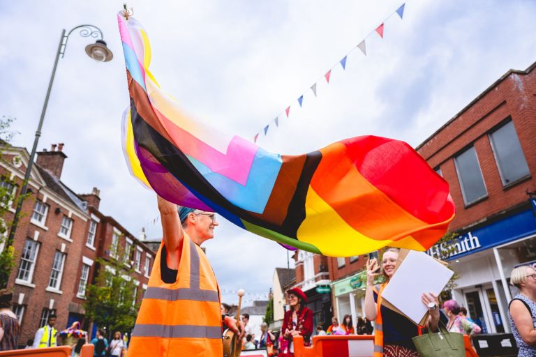A large Progress Pride flag is carried high above the Leek parade