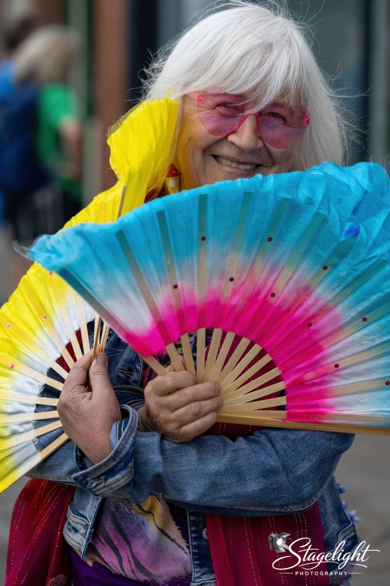 A marcher with rainbow glasses and colourful hand fans in Leek