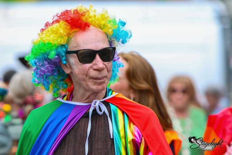 A marcher in a rainbow wig, sunglasses and rainbow cape in Leek